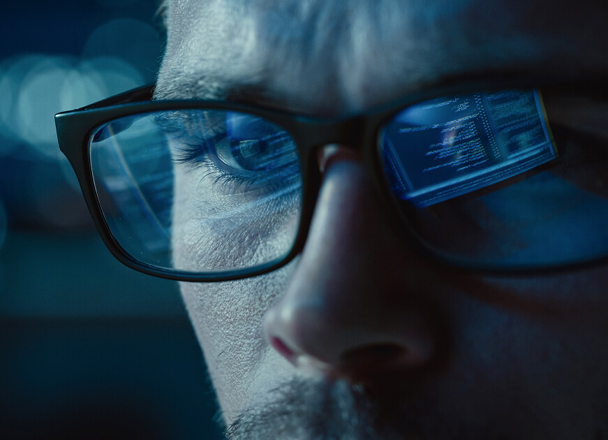 Close-up of a person’s glasses reflecting computer code on the screen.