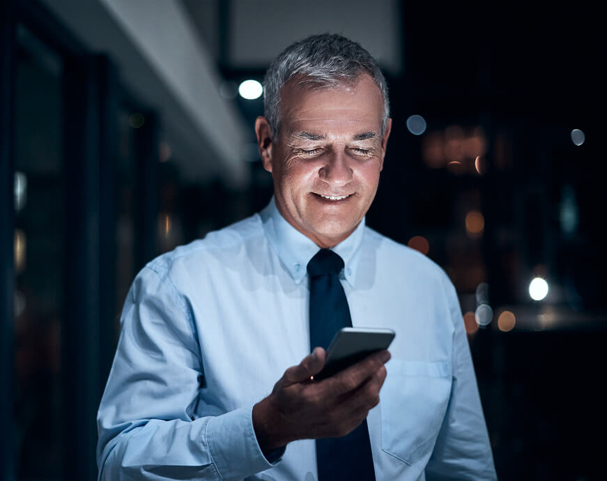 A businessman working late and smiling while looking at his phone.
