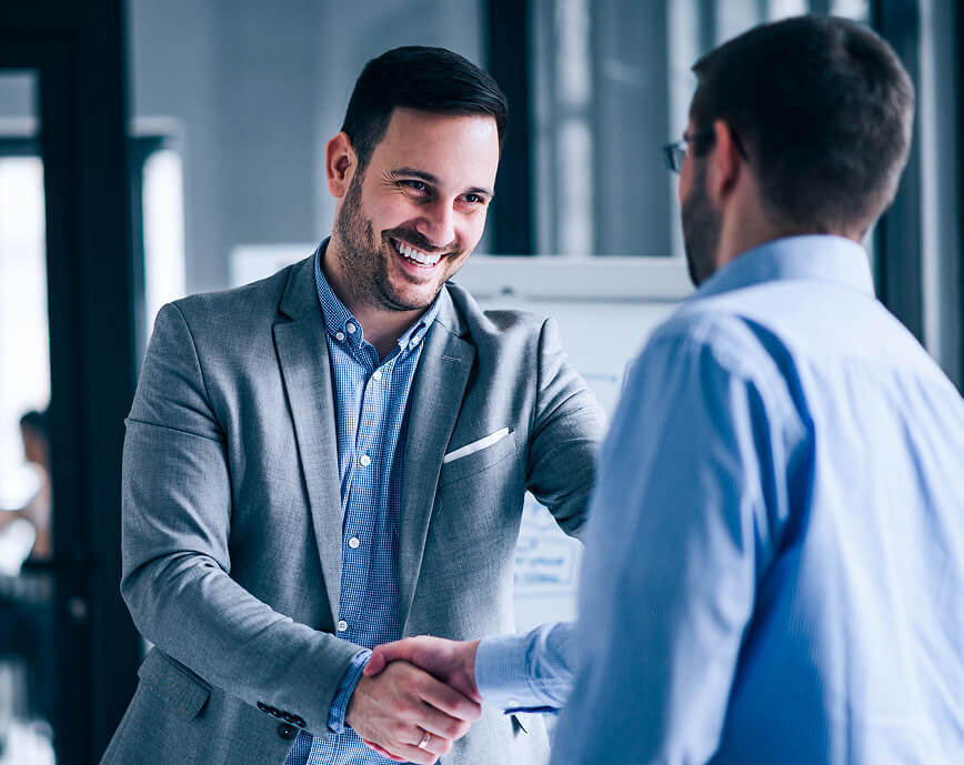 Two businessmen smiling and shaking hands warmly.
