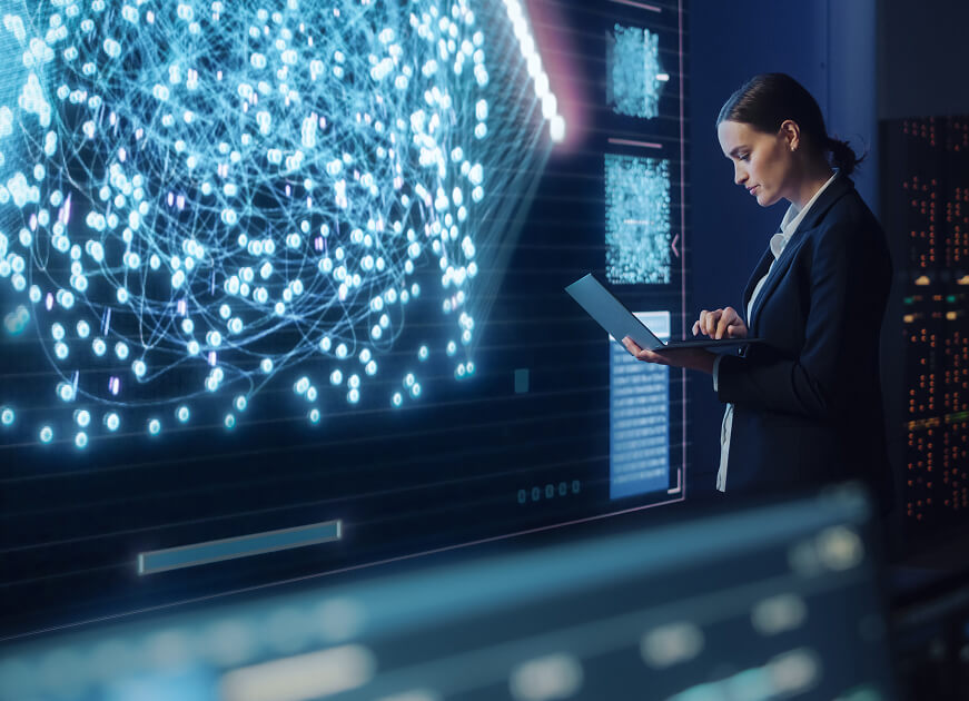 Business professional analyzing a large digital network visualization on a screen while working on a laptop.