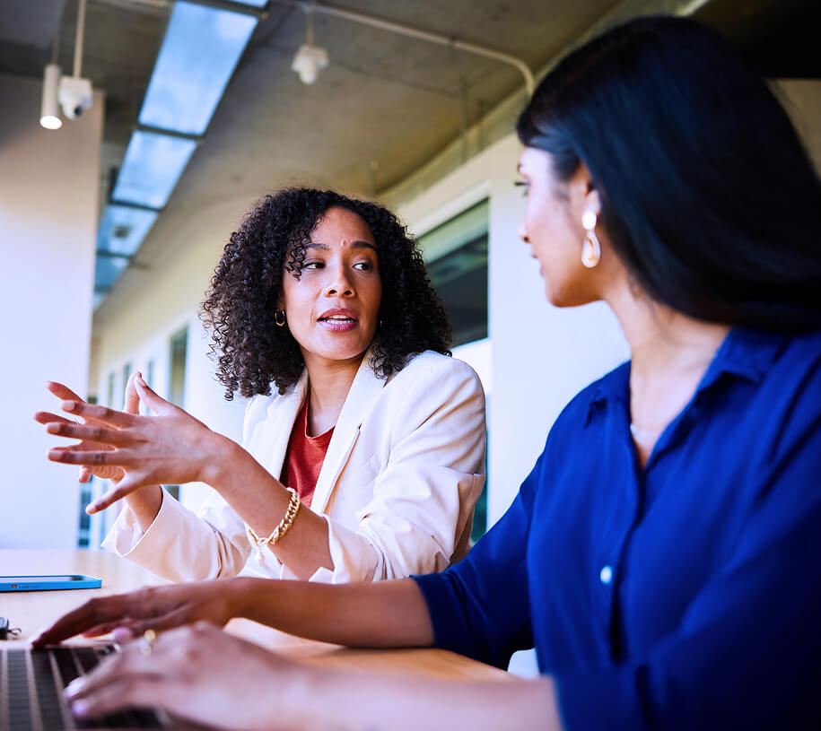 Two businesswomen having an animated conversation in a brightly lit office environment.