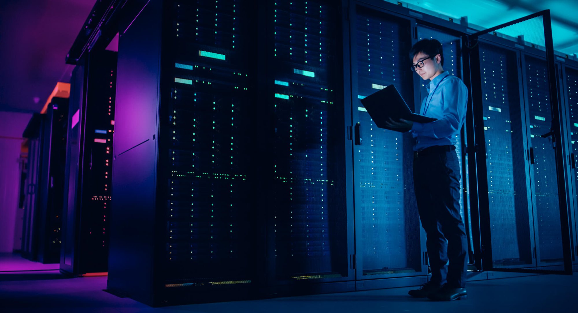 A professional man in a server room looking at his laptop.