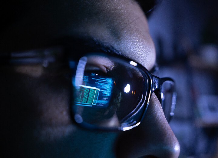 Close-up of man with glasses and a computer screen reflected in one lens.