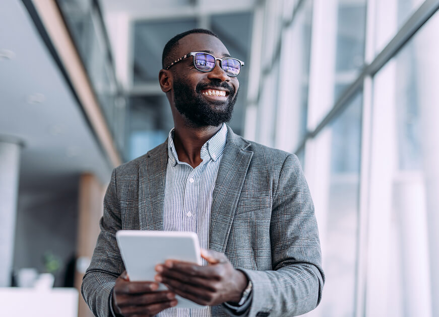 Smiling business professional holding a tablet in a modern office hallway.