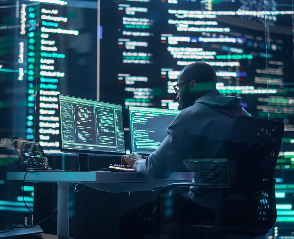 Person working at multiple monitors with code displayed on the screens.