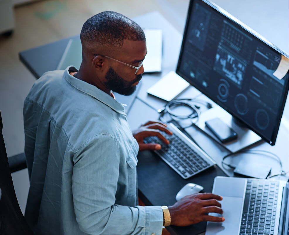 Professional working at a desk with multiple monitors displaying digital dashboards.
