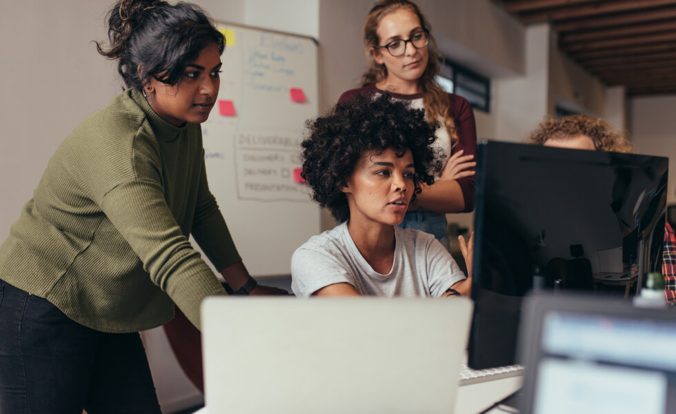 Group of mostly female, multiethnic young working professionals discussing idea on computer screen