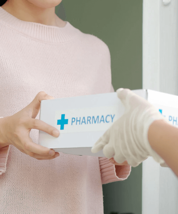 Person receiving a pharmacy package from a gloved hand, representing medication delivery or prescription service.