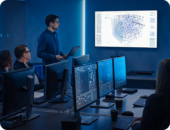 Team in a control room reviewing data on large monitors while a presenter explains visuals on a screen.