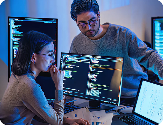 Two software developers reviewing code on multiple monitors in an office setting.