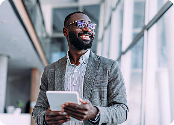 Smiling business professional holding a tablet in a modern office hallway.