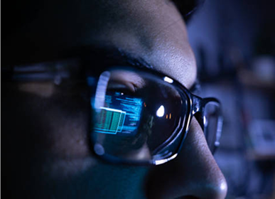 Close-up of eyeglasses with computer code reflected on the lens.