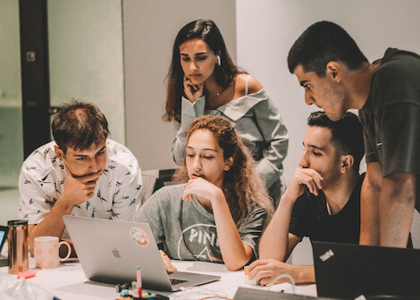 Five young working professionals huddled over laptop