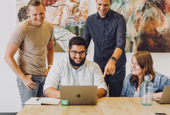 Team of professionals working together in an office referencing a laptop.