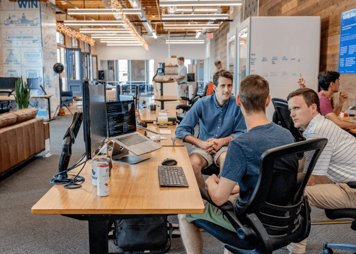 Trio of white men having a casual work discussion at their desk