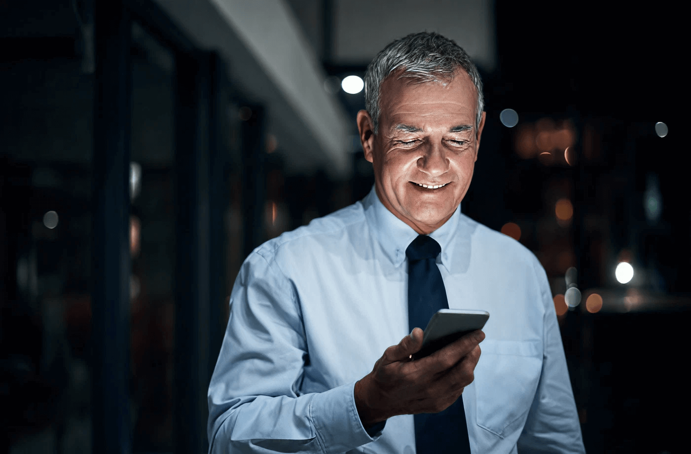 Business professional smiling while reading a message on a smartphone at night.
