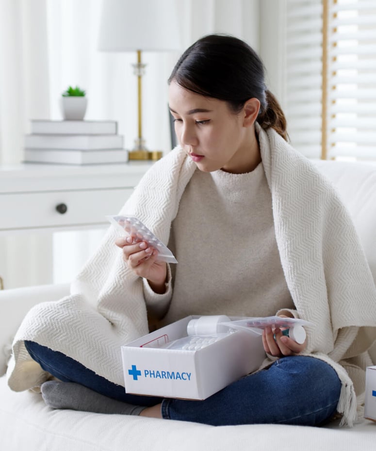 Young woman sitting on bed looking at package of pills from her pharmacy box