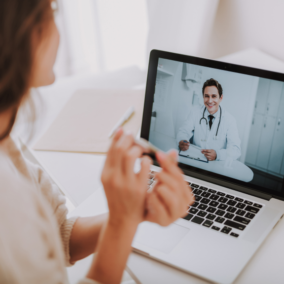 Woman checking in with male doctor via telehealth appointment on her laptop