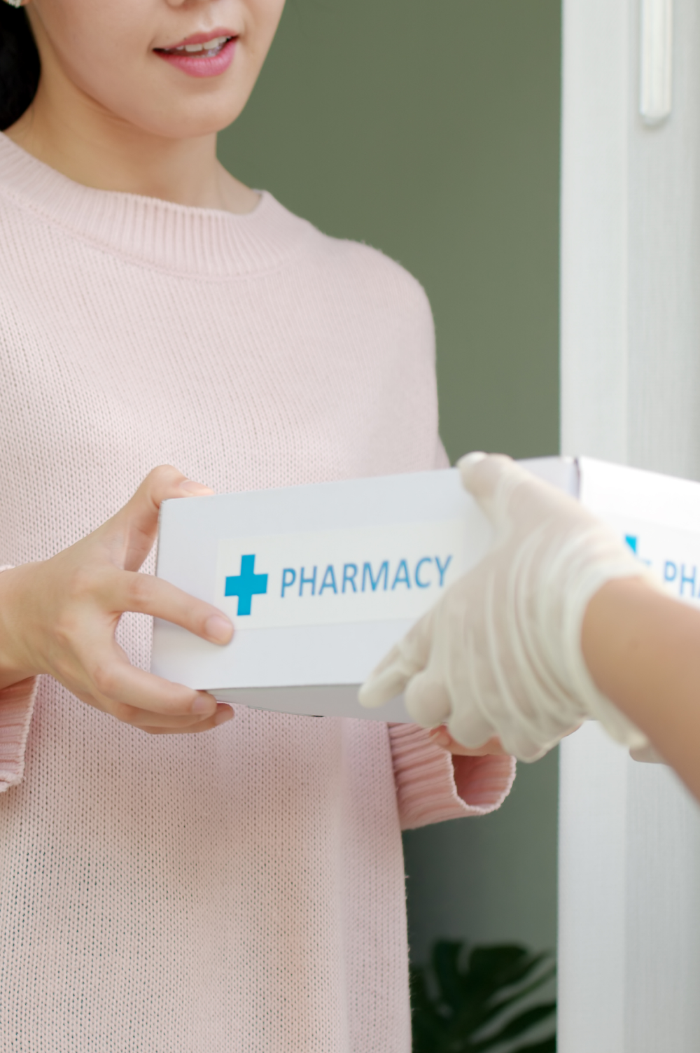 Woman receiving pharmacy subscription box from delivery person wearing gloves